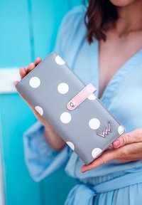 Gray wallet with large white polka dots, pink snap closure, and metal accent. Smooth texture, rectangular shape.