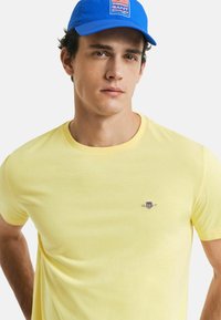 Yellow cotton t-shirt with a round neckline and short sleeves, featuring a small embroidered logo on the chest.