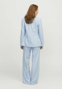 Hellblaues maßgeschneidertes Sakkos mit einem ausgestellten Design, kombiniert mit weit geschnittenen Hosen; glattes Gewebe und strukturierte Silhouette.