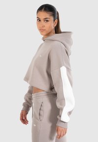 Geknipte beige hoodie van sweatshirtstof, met een witte accentstreep op de mouw en elastische manchetten, gecombineerd met bijpassende joggers.