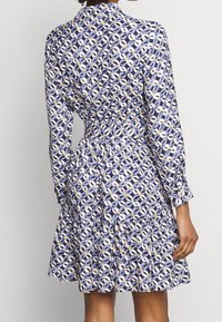 Blå mönstrad klänning med krage, långa ärmar, åtsittande midja och utställd nederdel med ett lager volang. Tillverkad av lättviktsmaterial.