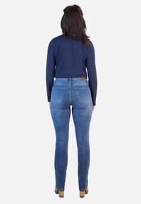 Vaqueros de tiro alto de color azul con dos bolsillos traseros, hechos de mezclilla, con una textura suave y un corte ajustado. Combinados con una blusa de manga larga en color navy.