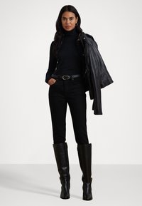 Zwarte turtleneck, hoge zwarte jeans en zwarte leren laarzen tot de knie. Een zwart leren jasje wordt over de schouder gehouden.