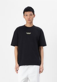 Tricou din bumbac negru cu mâneci scurte, având un mic logo alb și auriu "Hollister" pe piept, guler rotund, croială lejeră.