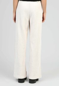 Pantalons larges crème en tissu doux et texturé. Présentent une taille lisse et des poignets ourlés. Se marient bien avec différentes chaussures.
