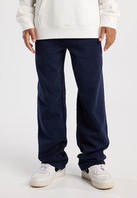 Navy blue relaxed-fit pants made of soft fabric, featuring a simple design and wide leg, paired with white sneakers.