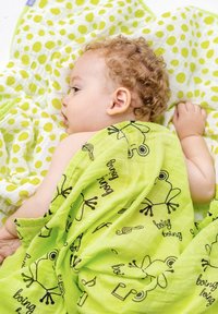 Green blanket featuring frog patterns and text, layered over a yellow and white polka-dot blanket. Soft, textured fabric shown.