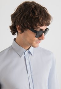 Gafas de sol rectangulares negras y una camisa de botones azul claro con cuello puntiagudo, textura suave y cierre delantero estándar.