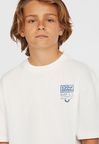Witte katoen T-shirt met een blauwe grafische print op het linkerbovenlichaam, ronde hals en korte mouwen. Subtiele textuur en losse pasvorm.