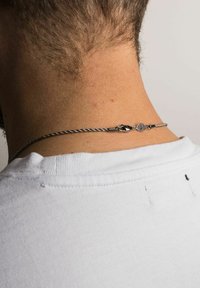 Colier din metal cu un design răsucit, având un închizător decorativ și un accent cu un model, purtat la baza gâtului unei persoane.