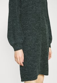 Mörkgrön stickad klänning med strukturerad yta, med långa puffärmar och rak passform, som når till mitten av låret.