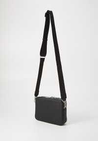 Bolso bandolera de cuero negro con un acabado texturizado, que presenta un cierre de cremallera y una correa ajustable con marca en relieve.