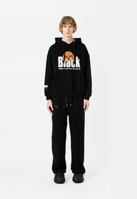 Sudadera negra con estampado gráfico, bolsillo canguro y capucha con cordón. Combinada con pantalones de chándal negros que cuentan con bolsillos laterales y un ajuste relajado.