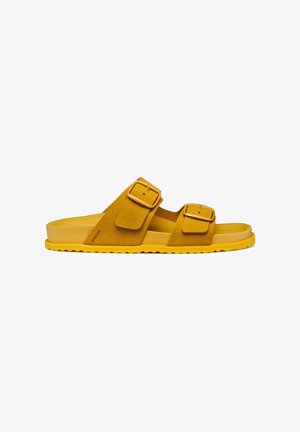 Sandali scivolati in suede giallo con due larghe cinghie regolabili e fibbie dorate. Presentano una suola in gomma spessa con un motivo a onde.