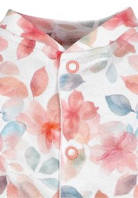 Gros plan sur un tissu à motifs floraux avec des boutons-pression roses sur fond blanc, montrant le col et une partie de l'avant du vêtement.