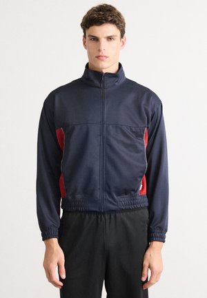 Marine atletisk jakke med røde sidestriper, høy krage, hel glidelås, elastiske mansjetter og midjebånd; laget av glatt, lett stoff.