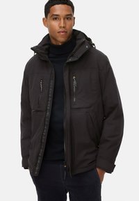 Schwarze Zip-Jacke mit Kapuze, ausgestattet mit zwei Frontreißverschlusstaschen, Seitentaschen und strukturierten Stoffdetails entlang des Reißverschlusses.