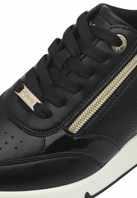 Sneaker nera con tomaia in pelle lucida e dettagli perforati, accento in zip dorata, lacci neri e suola in gomma bianca.