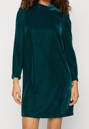 Zielononiebieska sukienka z aksamitu z wysokim dekoltem, długimi rękawami i marszczeniem po bokach. Materiał ma gładką fakturę i delikatny połysk.