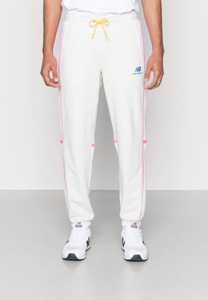 Mann trägt weiße Jogginghosen mit pinken Seitenstreifen, gelbem Kordelzug, New Balance Logo und weißen Sneakers mit roten Akzenten.