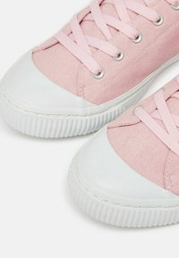 Rosa Leinenschuhe mit einer weißen Gummikappe und Sohle, ausgestattet mit einem tonal abgestimmten Schnürdesign und silbernen Ösen für die Schnürsenkel.