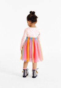 Långärmad topp med rosa prickar och en regnbågsfärgad tylskjol. Har lager av färgglada pom-pom detaljer. Svarta glittriga stövlar med rosa kant.