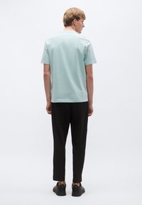 Hele sinine lühikeste varrukatega T-särk, millel on ümmargune kaelus; kangas tundub pehme ja vähe tekstuuriga, kombineeritud mustade kitsenevate pükstega.