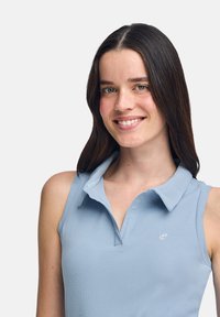 Ljusblå ribbad ärmlös polo med krage och delvis knappslå. Har en liten vit logotyp på bröstet.