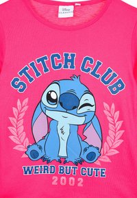 Rosa Baumwoll-T-Shirt mit einem blauen Cartoon-Charakter, der sitzt und zwinkert, mit den Aufschriften "STITCH CLUB" und "WEIRD BUT CUTE 2002" in fettem Text.