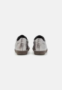 Scarpe in pelle argentata metallica con una forma arrotondata, dotate di una suola in gomma marrone e un marchio impresso sul tallone.