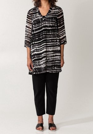 Tunique rayée noire et blanche à manches trois-quarts, coupe ample et col en V. Associée à un pantalon noir court et des sandales.