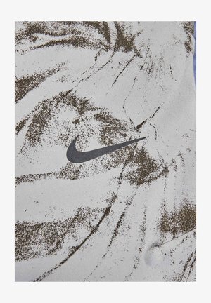 Nike Sportbekleidung mit einer strukturierten weißen Oberfläche, die mit braunen Farbspritzern versehen ist. Deutlich sichtbar ist das schwarze Nike-Logo.