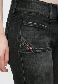 Mustad teksad kitsas lõikes, millel on iseloomulik kaldus tagatasku ja punase-musta kirjaga "Diesel Industry" silt.