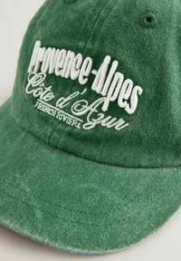 Grüne Cordmütze mit weißer Stickerei "Provence-Alpes Côte d'Azur Französische Riviera". Gebogener Schirm, strukturierter Stoff und Nähdetails.