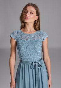 Helles blaues Spitzenkleid mit kurzen Ärmeln, floralem Muster und Paillettenakzenten. Satinband in der Taille, fließender Stoffrock.