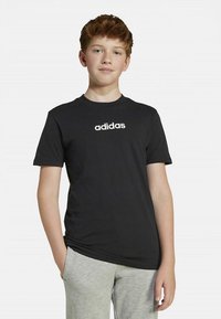 Mustast puuvillast T-särk lühikeste varrukatega, rinnal valge "adidas" logoga. Kanditud heledate hallide dressipükstega.