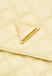 Żółty pikowany portfel z eko skóry z złotą trójkątną tabliczką z logo "GUESS" i wzorem znaku zapytania.