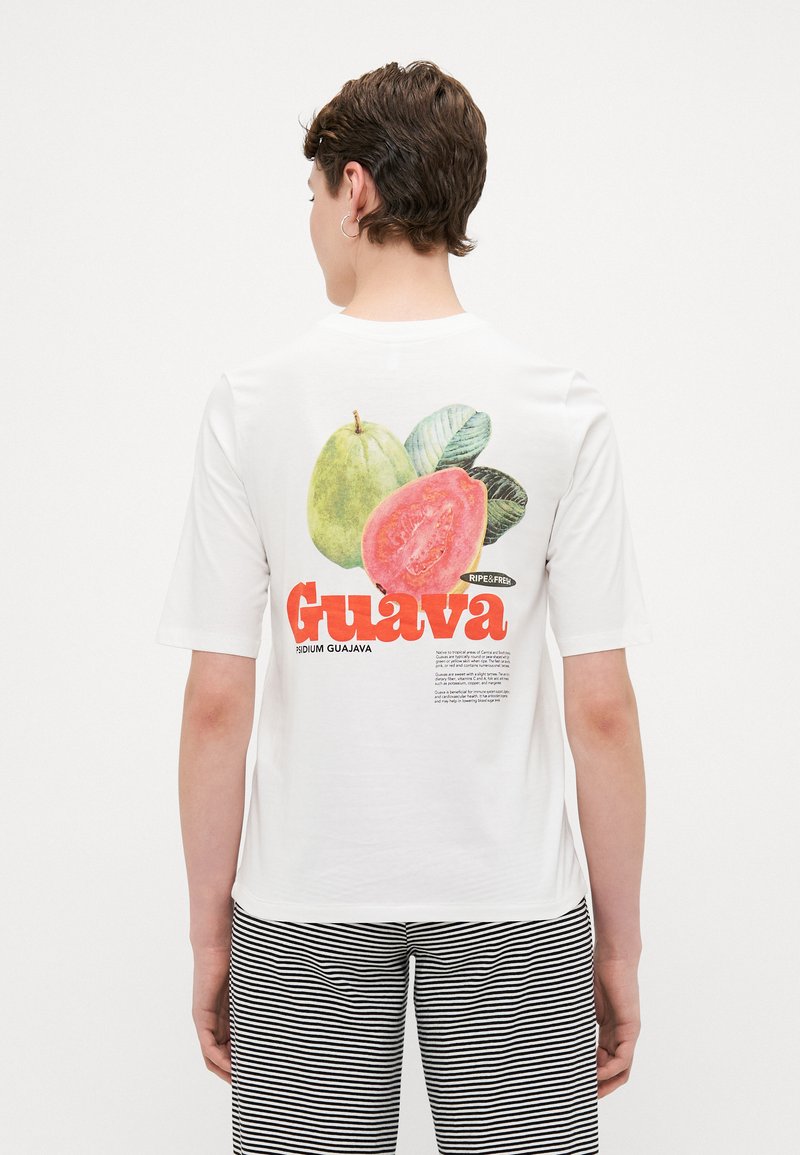 Hvid t-shirt med et farverigt guava-grafik på ryggen, med fed tekst "Guava" i rød og stiliserede frugtillustrationer. Stribede bukser.
