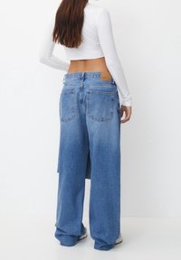 Jeans de caña ancha en azul claro, con una cinturilla alta, dos bolsillos traseros y una etiqueta de cuero marrón en la parte trasera.