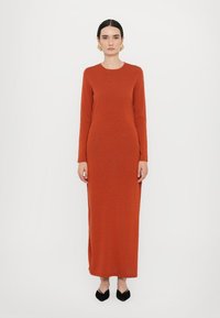 Långärmad, figurnära klänning i bränd orange stickad tyg. Golvlång med rund halsringning, kombinerad med svarta spetsiga ballerina skor. Minimalistisk design.