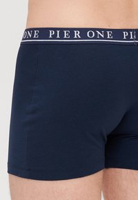 Sötétkék pamut boxer alsó, testhezálló fazonban, kontrasztos elasztikus derékpánttal, amelyen fehér betűkkel a "PIER ONE" felirat látható.
