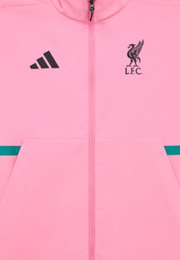 Roosa spordijakk musta adidas logoga ja Liverpool FC embleemiga. Omab täissilindrit, kahte taskut ja türkiissiniseid horisontaaltriibu.