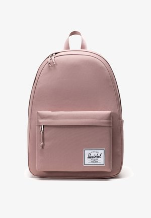 Sac à dos en tissu rose avec un compartiment principal zippé, une poche avant et une poignée sur le dessus. Présente un logo de marque et un matériau à texture lisse.
