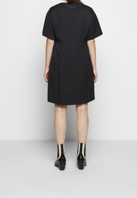 Svart kortärmad klänning med lös passform, med rund halsringning och diskret sömnad bak. Matchas med svarta och krämfärgade ankelskängor.