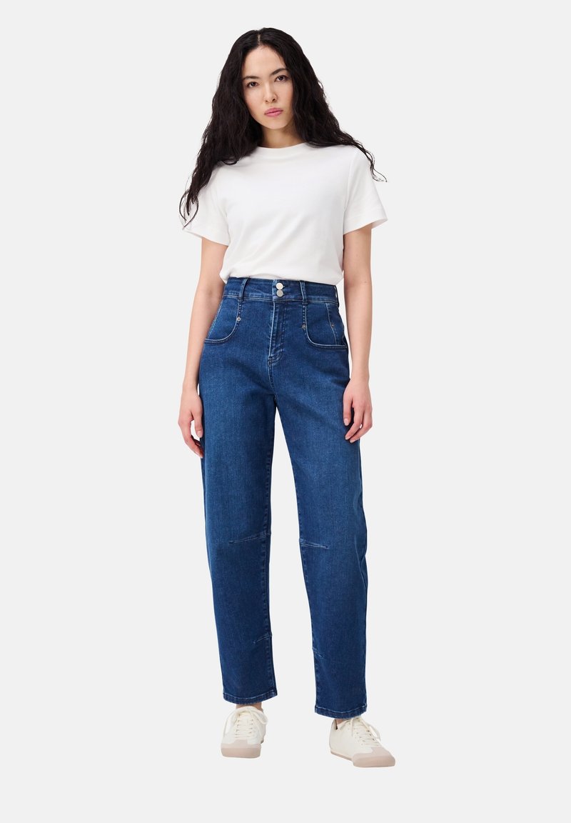 Dunkelblaue Jeans im High-Waist-Stil aus Denim mit zwei Vorderseiten Taschen, sichtbaren Nähten und einem Zwei-Knopf-Verschluss. Kombiniert mit einem schlichten weißen T-Shirt.