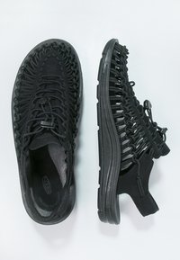 Zwarte atletiekschoenen met een bovenwerk van geweven materiaal, rubberen zool, gebogen vorm en verstelbare veterkoord voor een stevige pasvorm.