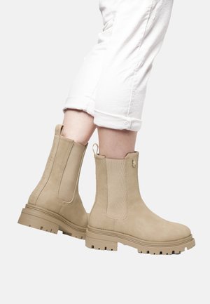 Botas de tobillo beige con una textura suave similar al ante. Paneles laterales elásticos y una suela de goma con un patrón. Forma cónica con un lazo de tirón.