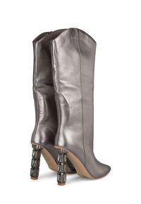 Bottes métalliques argentées montantes au design épuré, bout pointu et talon détaillé de manière géométrique unique. Texture lisse et forme ajustée.