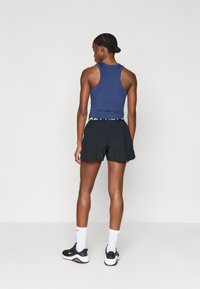 Ναυτικό αμάνικο φανελάκι σε συνδυασμό με μαύρα σορτς που διαθέτουν ελαστική ζώνη με λογότυπο. Λευκές κάλτσες τύπου crew και μαύρα αθλητικά παπούτσια ολοκληρώνουν την εμφάνιση.