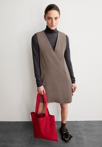 Braunes Cordkleid mit tiefem V-Ausschnitt, über einem schwarz-gestreiften Rollkragenpullover in grau und schwarz. Rote Tragetasche, schwarze Fransen-Schuhe und braune Socken.